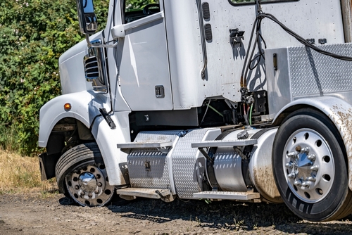 Damaged white semi-truck with a blown front tire on a dirt roadside, representing the aftermath of a truck accident and mechanical failure.