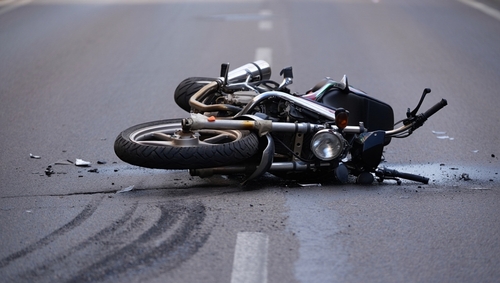 A damaged motorcycle lying on its side in the middle of a road after an accident, with skid marks and debris visible around it.