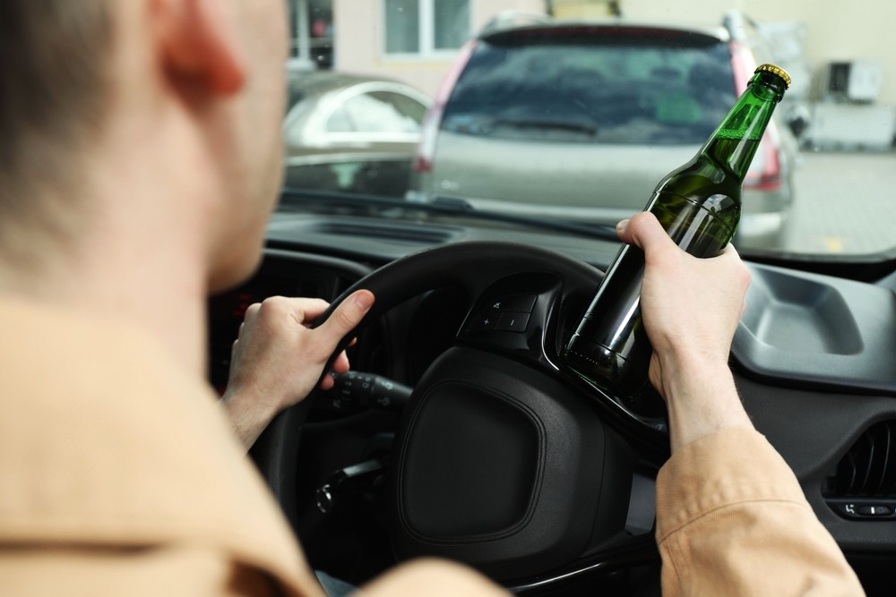 Driver holding a beer bottle behind the wheel of a car in a parking lot