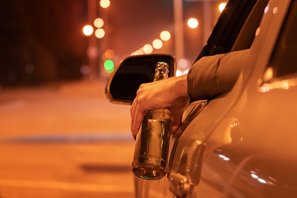 Drunk man driving a car with a bottle of beer at the night. Don't drink and drive concept.